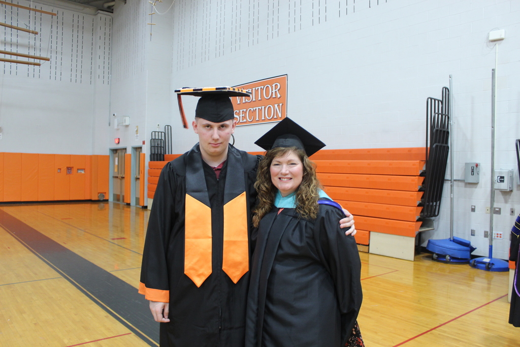 stduent standing next to woman in graduation caps and gowns