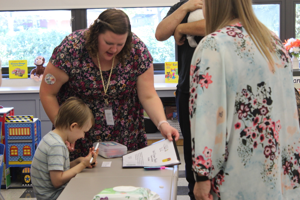 teacher helping student at desk while parents stand nearby