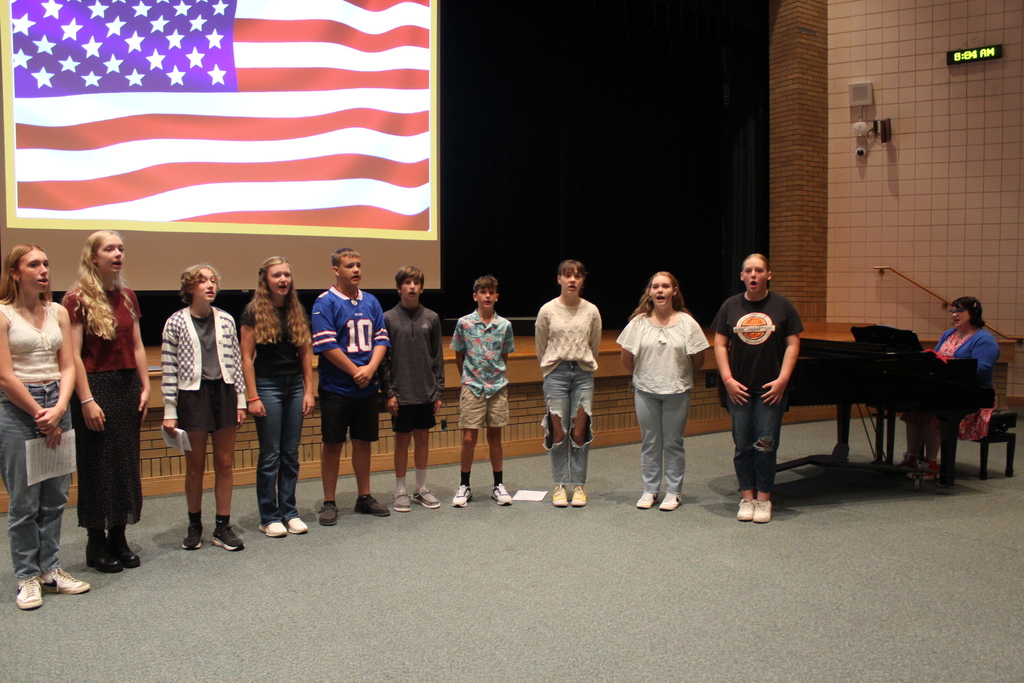 students standing singing in front of piano