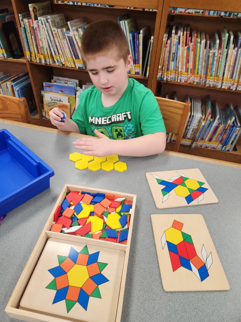 a boy sitting at a table building a puzzle with shapes
