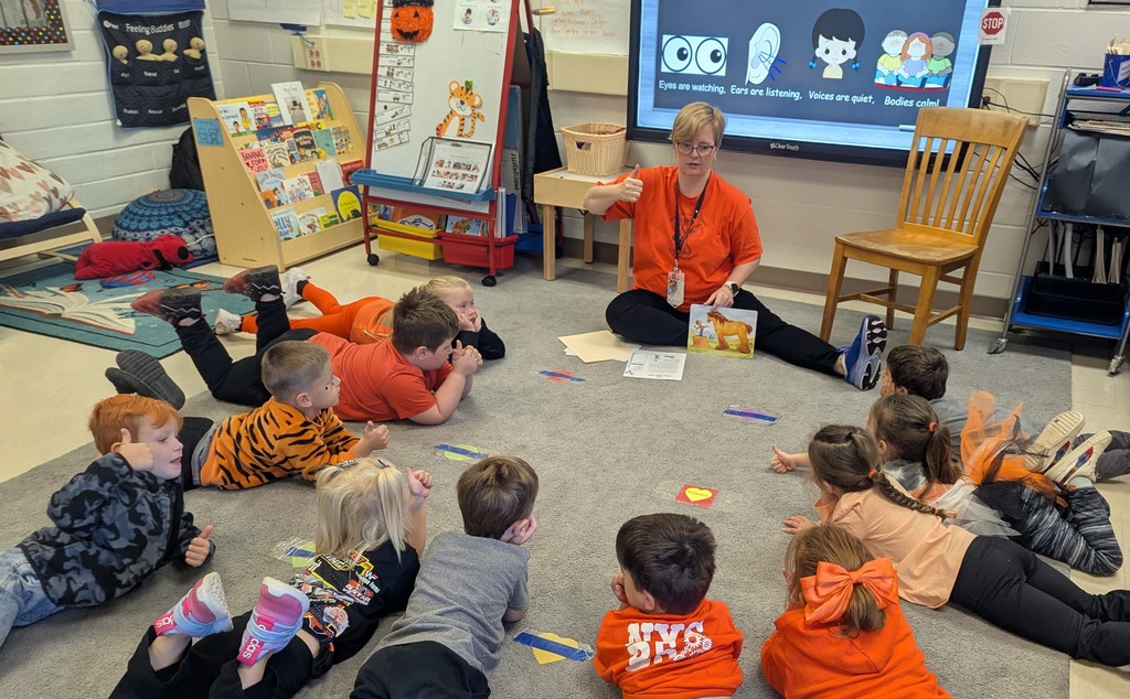 students lying on rug in classroom listening to teacher