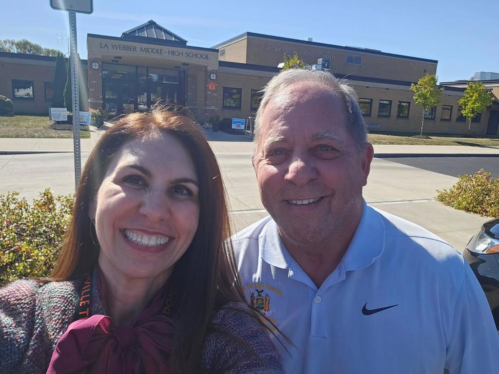 two adults standing together in front of a school
