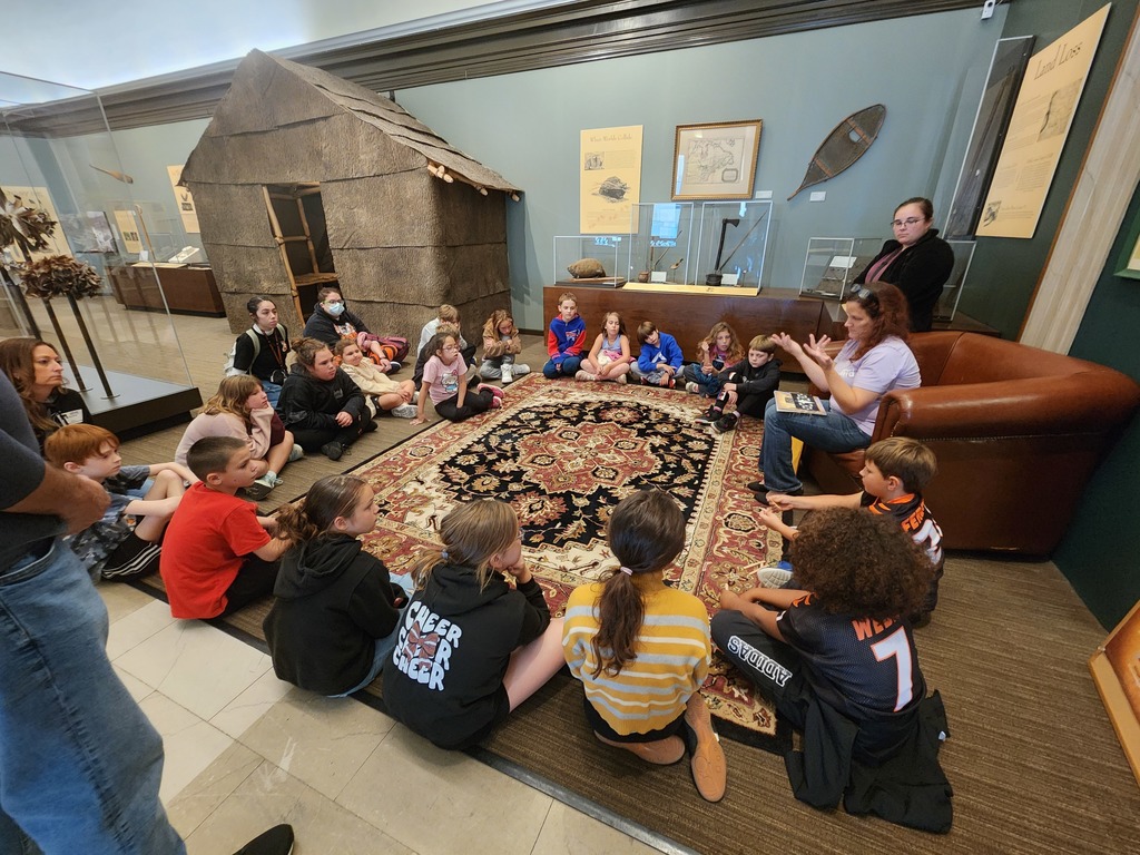 students sitting on rug in museum listening to speaker