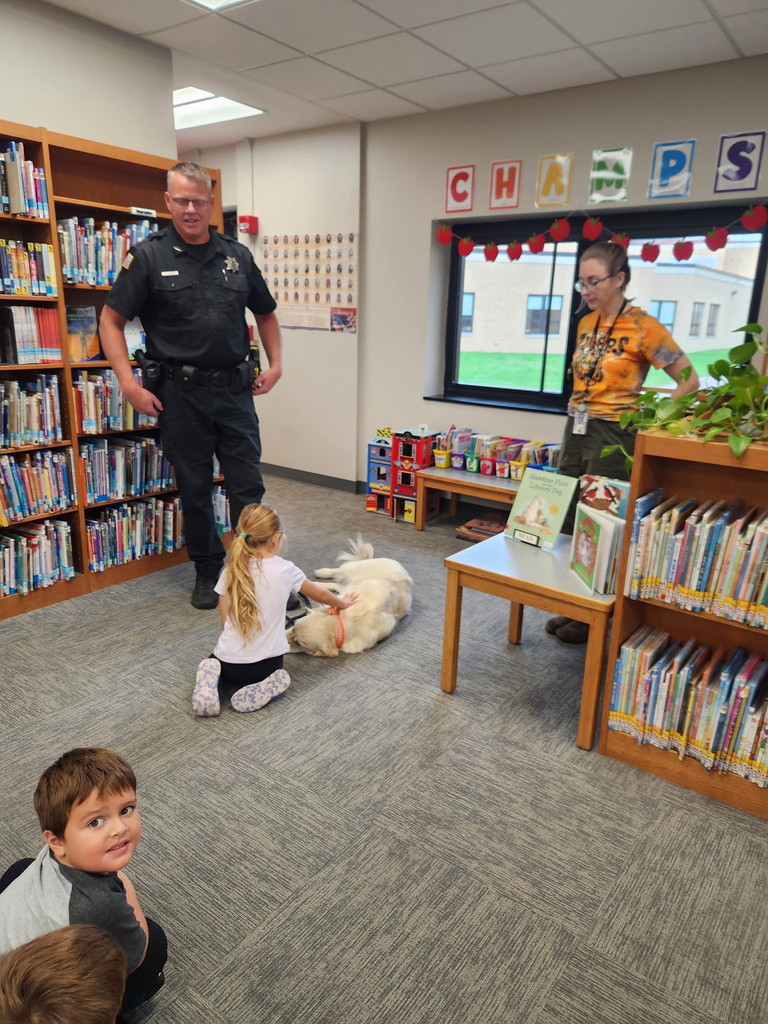 girl petting dog lying on library floor next to sheriff deputy