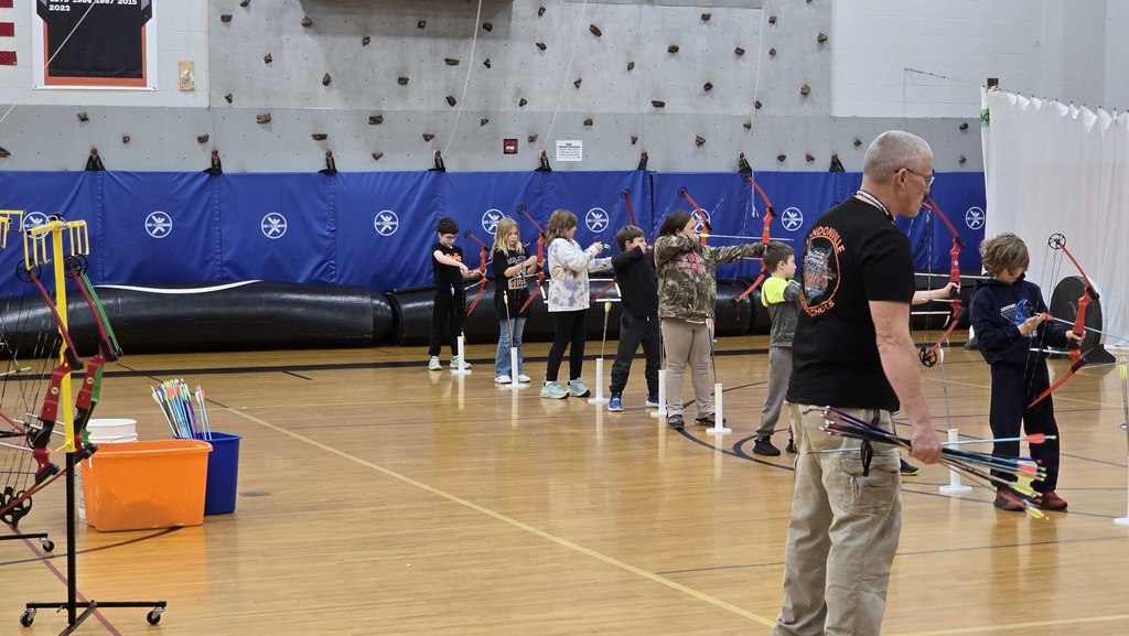student using bows and arrows in gym with instructor supervising