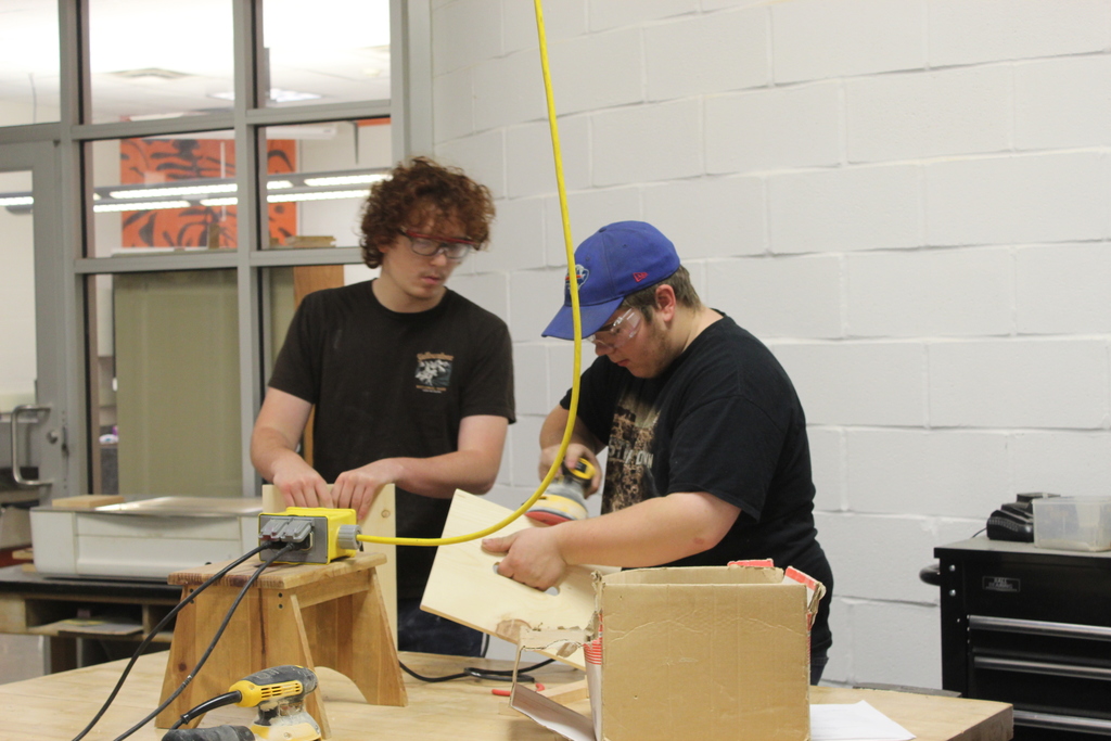 two boys working on wooden stool pieces in workshop