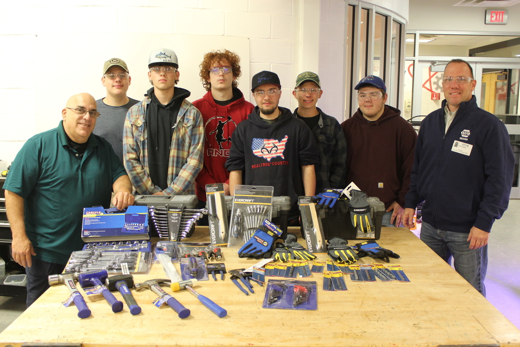 students and adults stand around table displaying tools