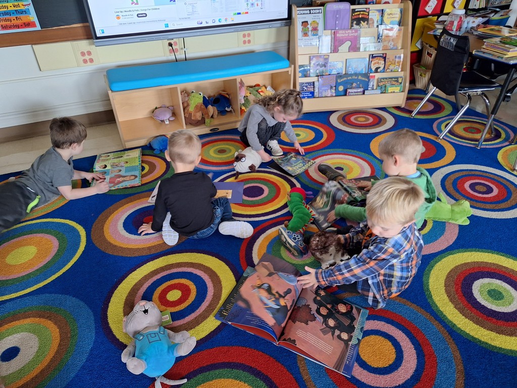 students sitting on the carpet reading books to stuffed animals