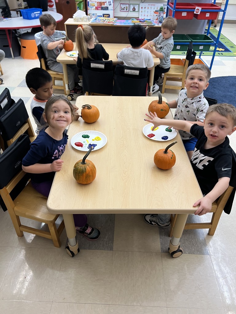 students seated at table painting their pumpkins