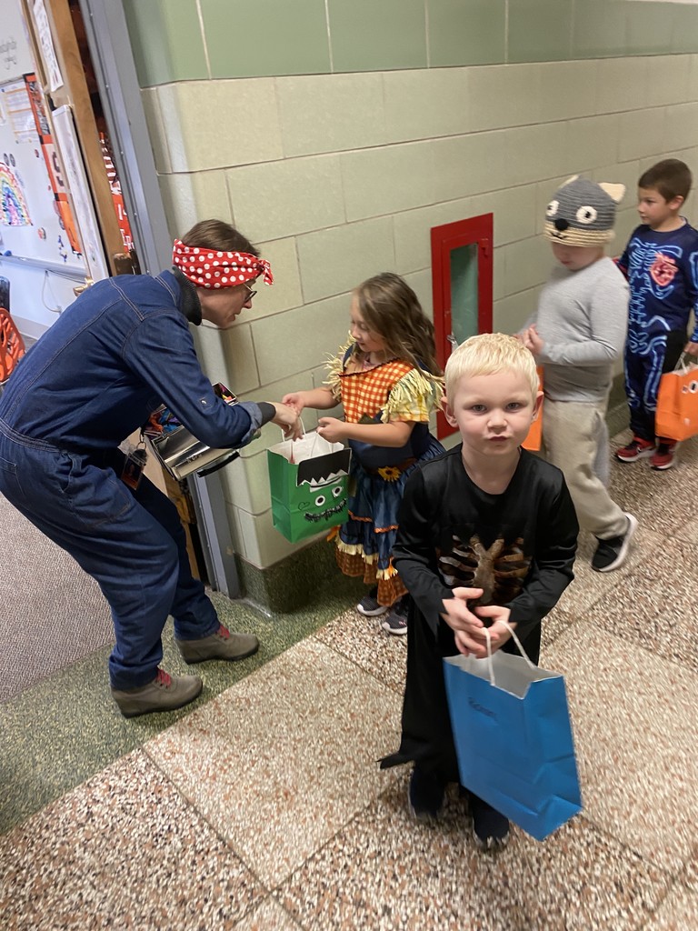 students trick or treating in hallway and receiving candy in their bags from adult