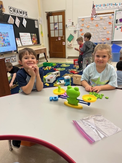 two students sitting at table with objects in front of them