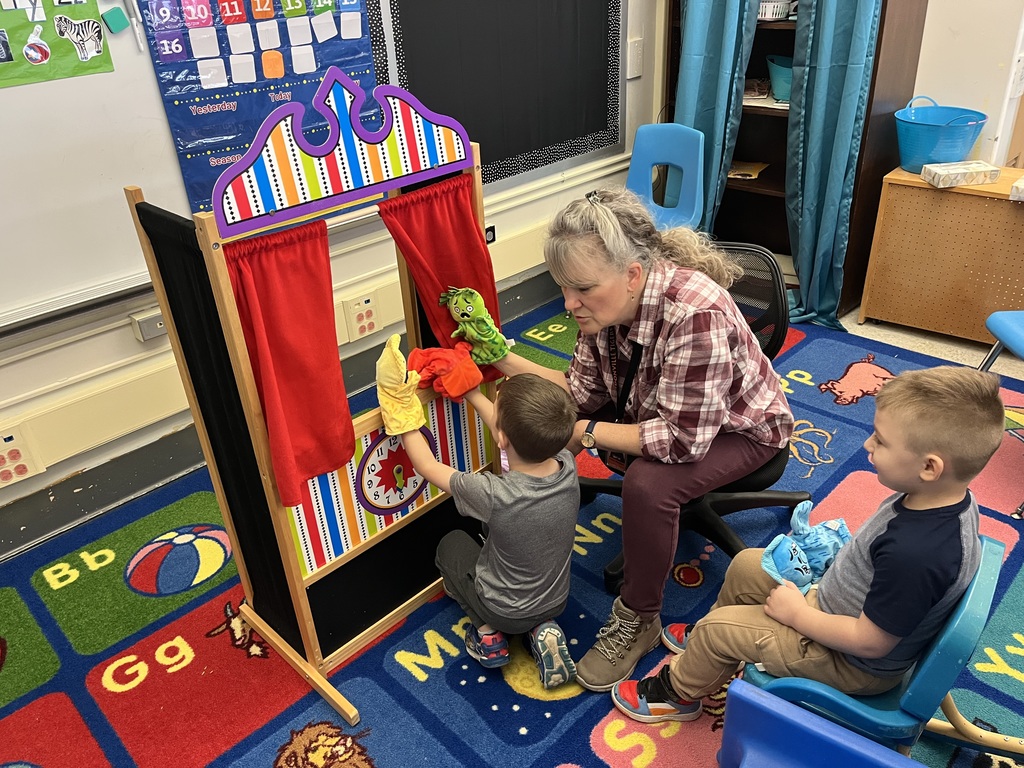student playing puppets with teacher while another student watches