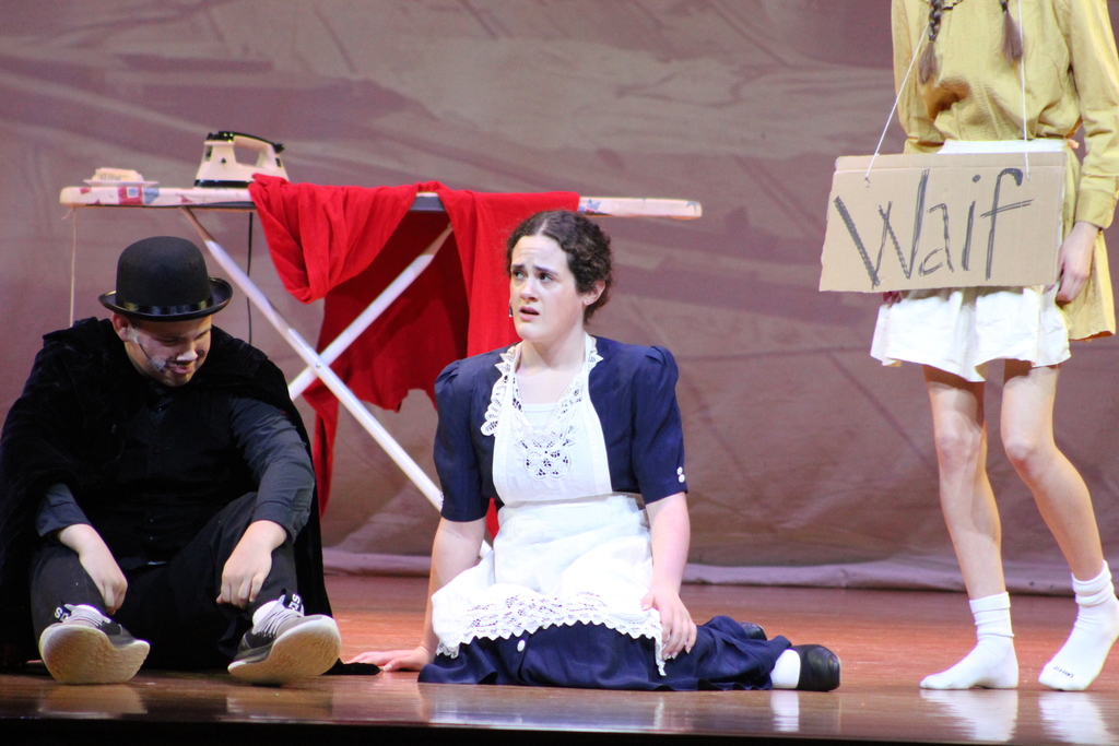 two students sitting on stage floor while one student stands