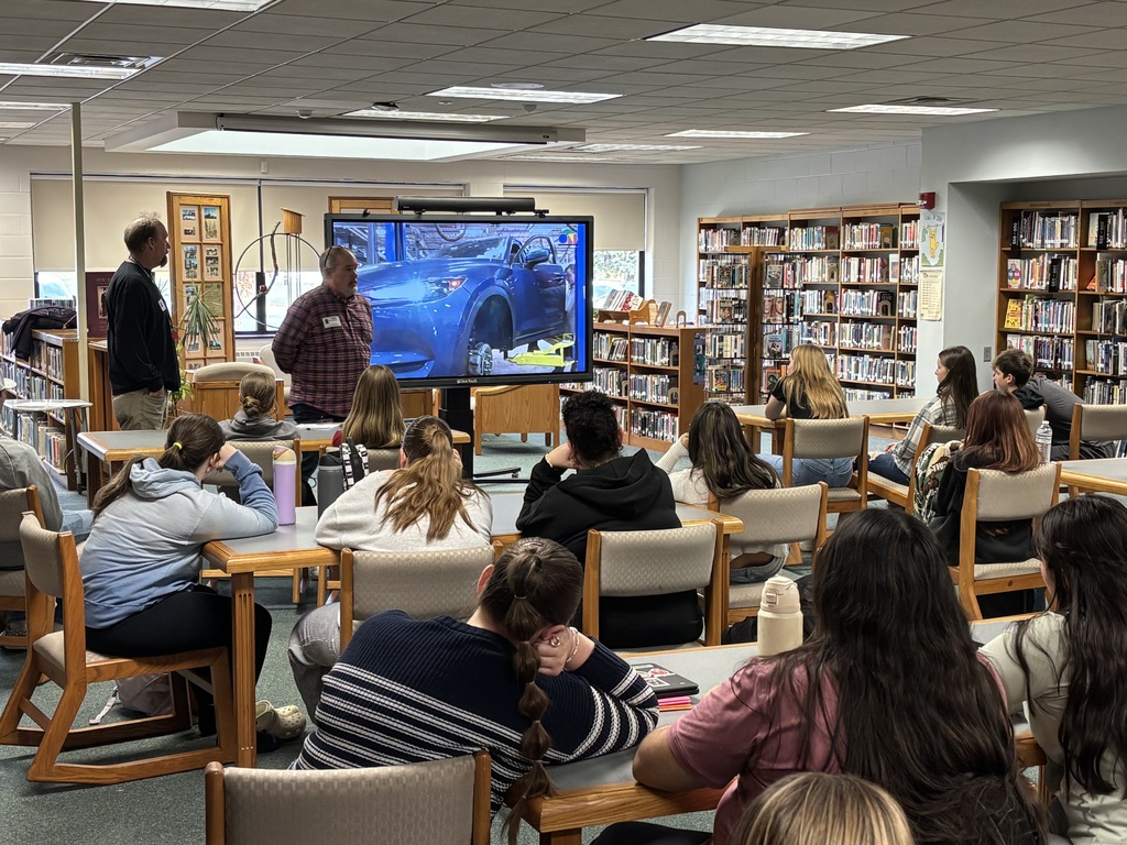 students seated at tables in library watching a presentation