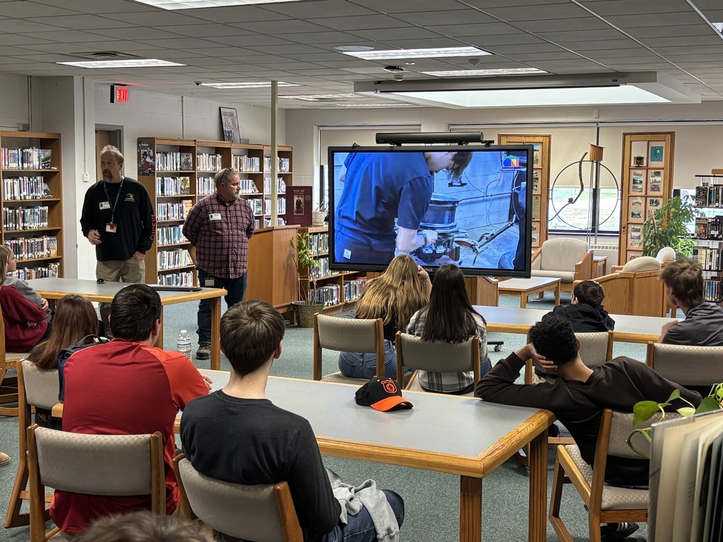 students seated at tables in library watching a presentation