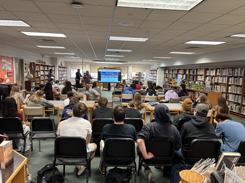 students seated at tables in library watching a presentation
