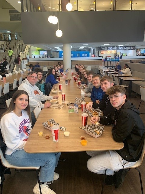 students and staff seated at a table in a dining hall