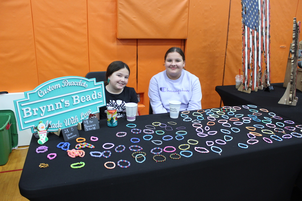 two girls sitting behind a table full of bracelets