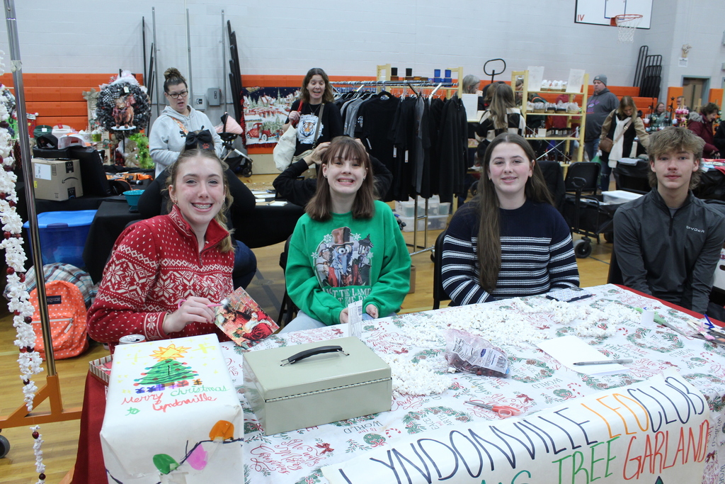 four students seated behind a table with a popcorn chain