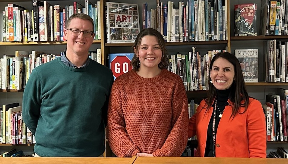 three adults standing in library