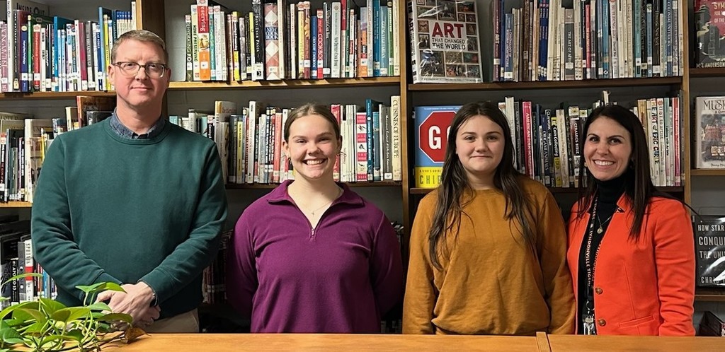 two adults and two students standing together in the library