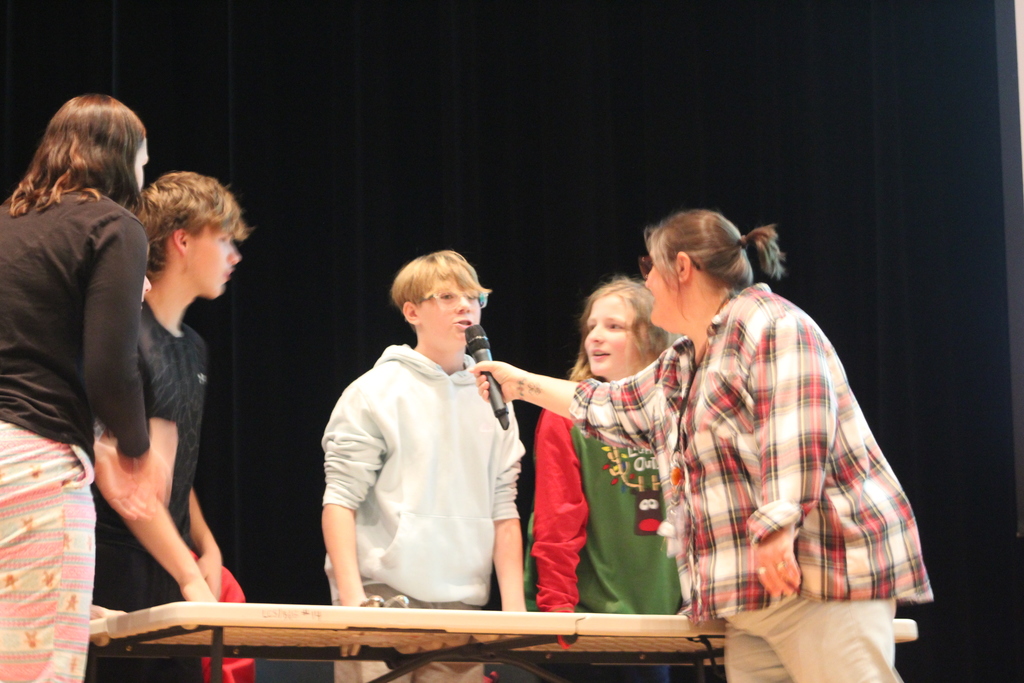 student talking into a microphone adult is holding with other students standing around a table