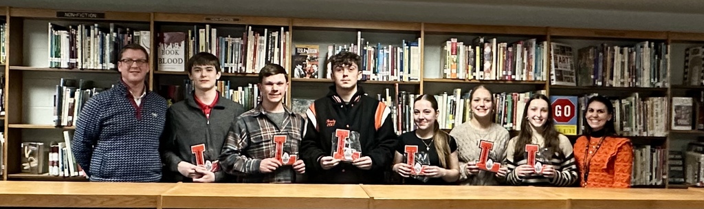 adults and students holding letters standing in the library