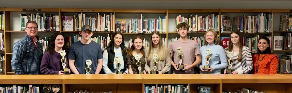 adults and students holding trophies standing in the library