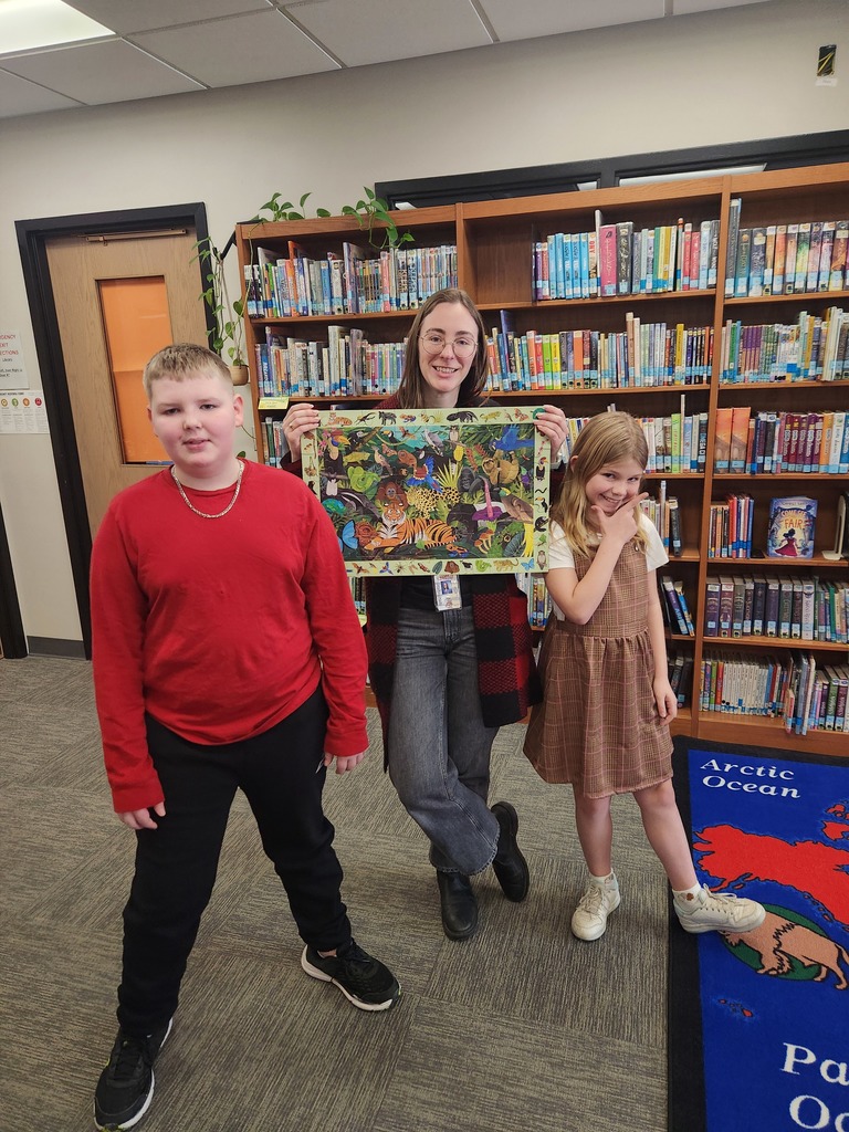 two students and adult holding puzzle in library