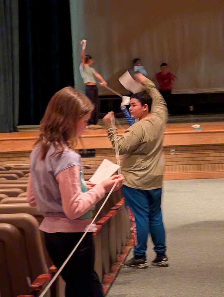 students in auditorium holding up string and paper