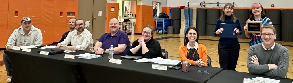 advisor and student standing behind board of educaition members seated at table with school superintendent