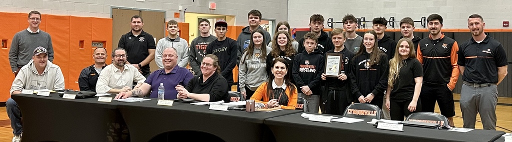 wrestling team standing behind board of educaition members seated at table with school superintendent