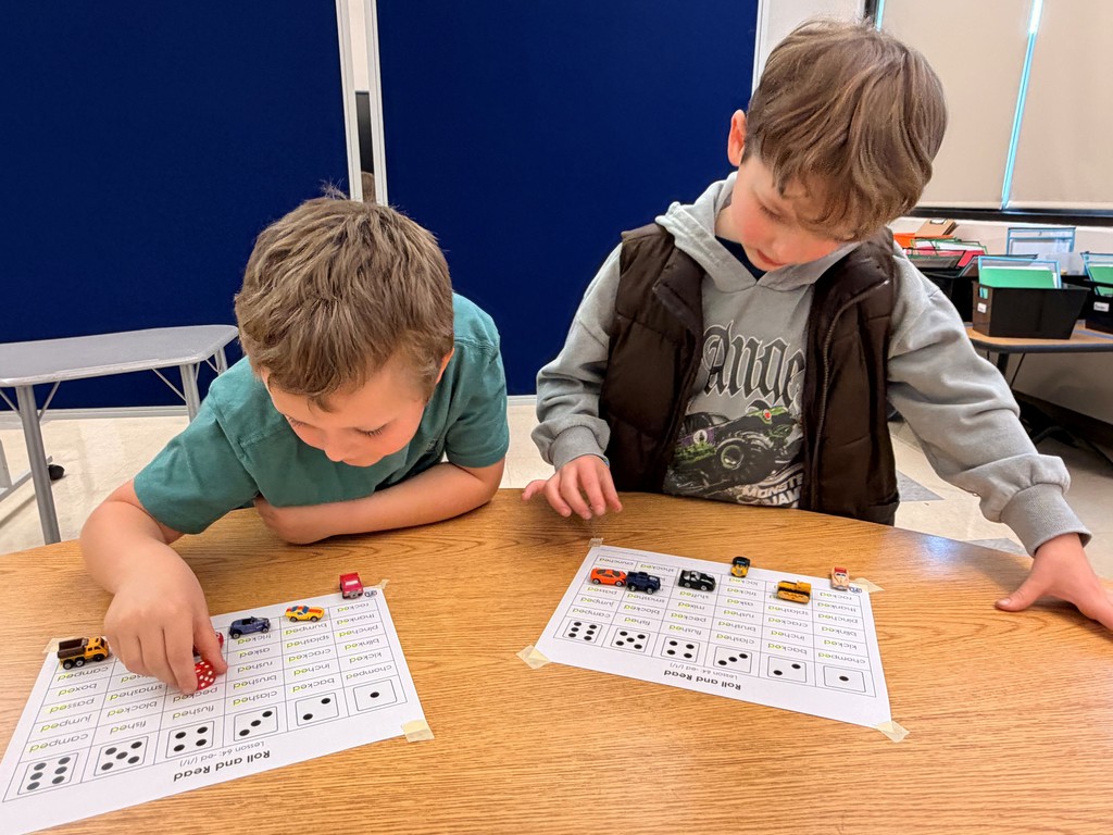 two boys completing worksheets with toy cars