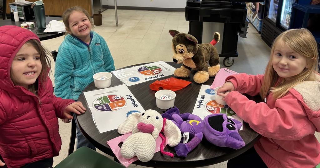 three students sitting at table with their stuffed animals