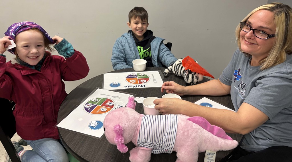 two stufents and adult sitting at table with stuffed animals