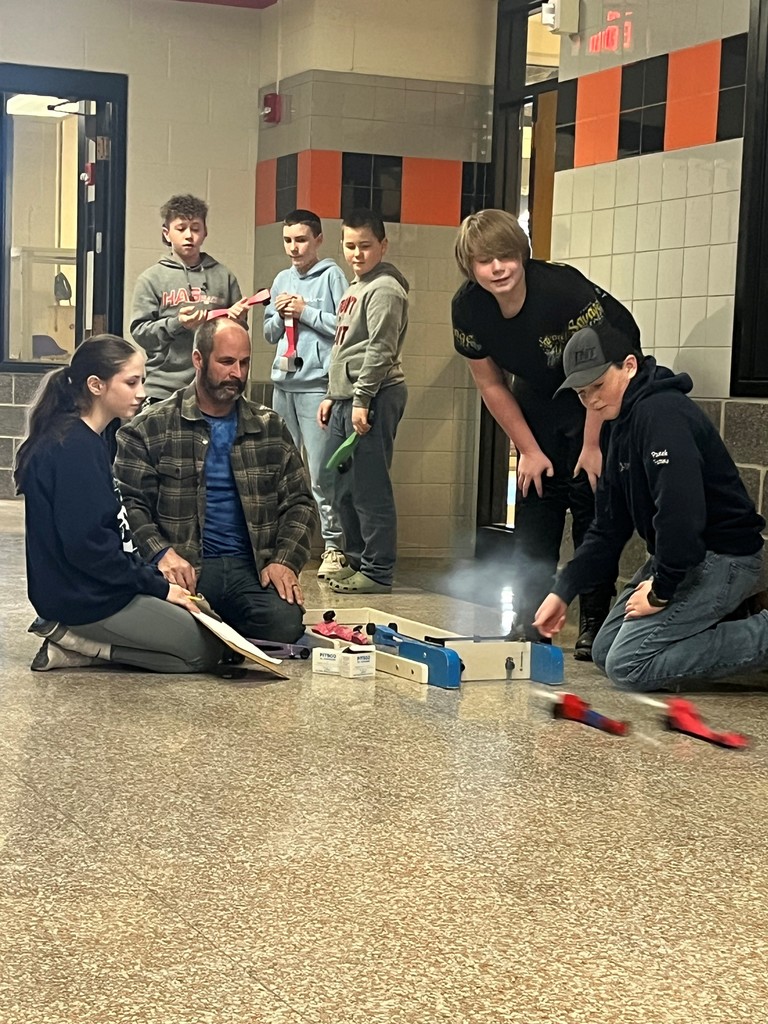 students racing CO2 cars with teacher down a ramp in hallway