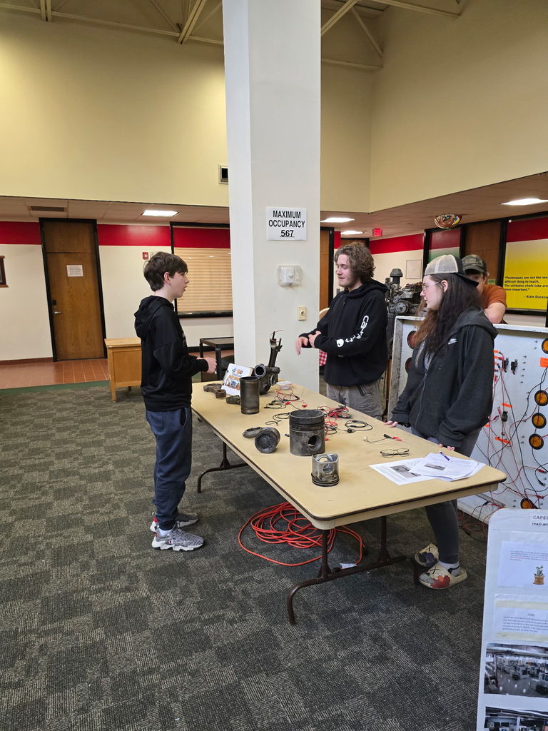 student talking to two students behind a table about their display