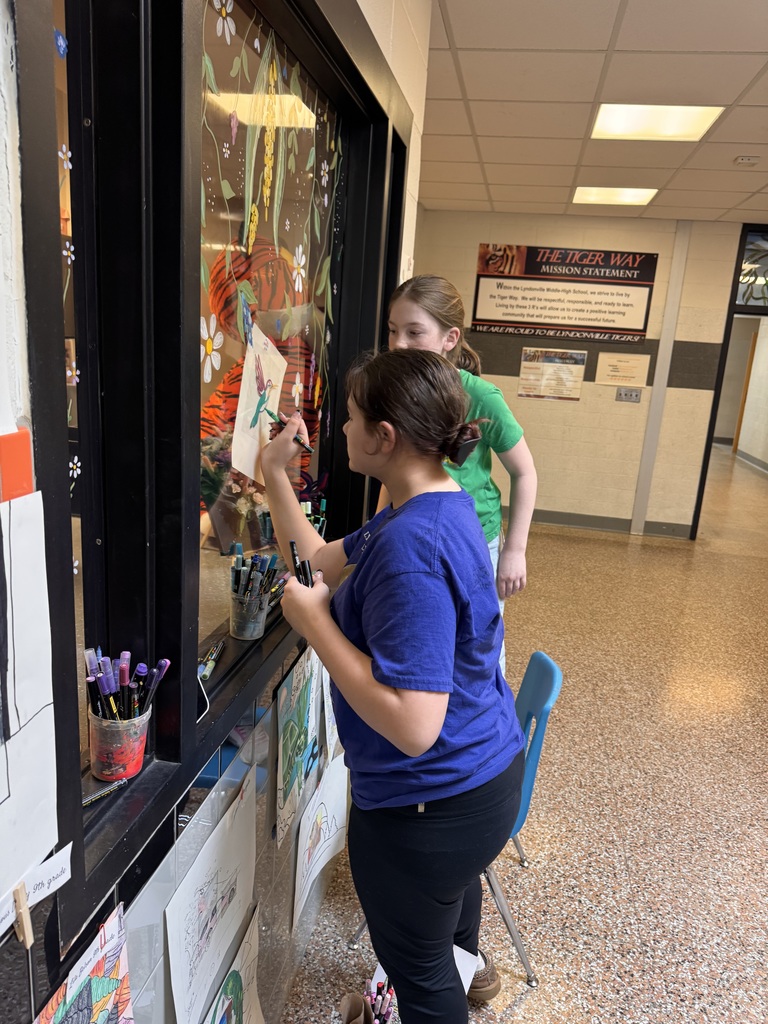 two students painting window outside main office