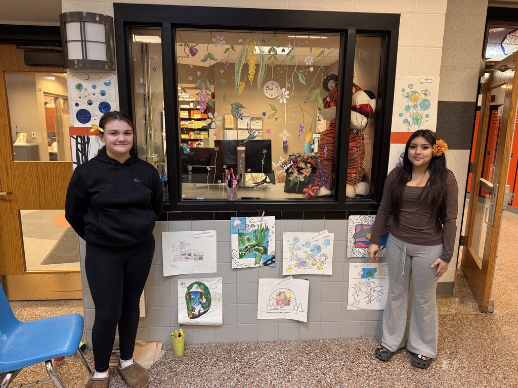 two students outside window of main office with art on display