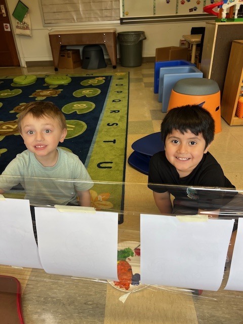two boys sitting on the floor with paint and worksheets