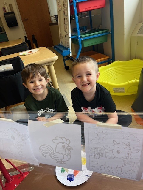 two boys sitting on the floor with paint and worksheets