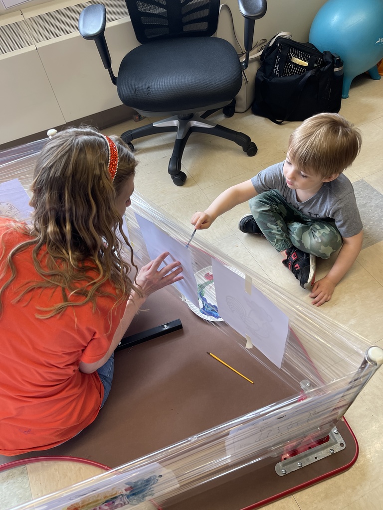 student and teacher sitting on the floor with paint and worksheets