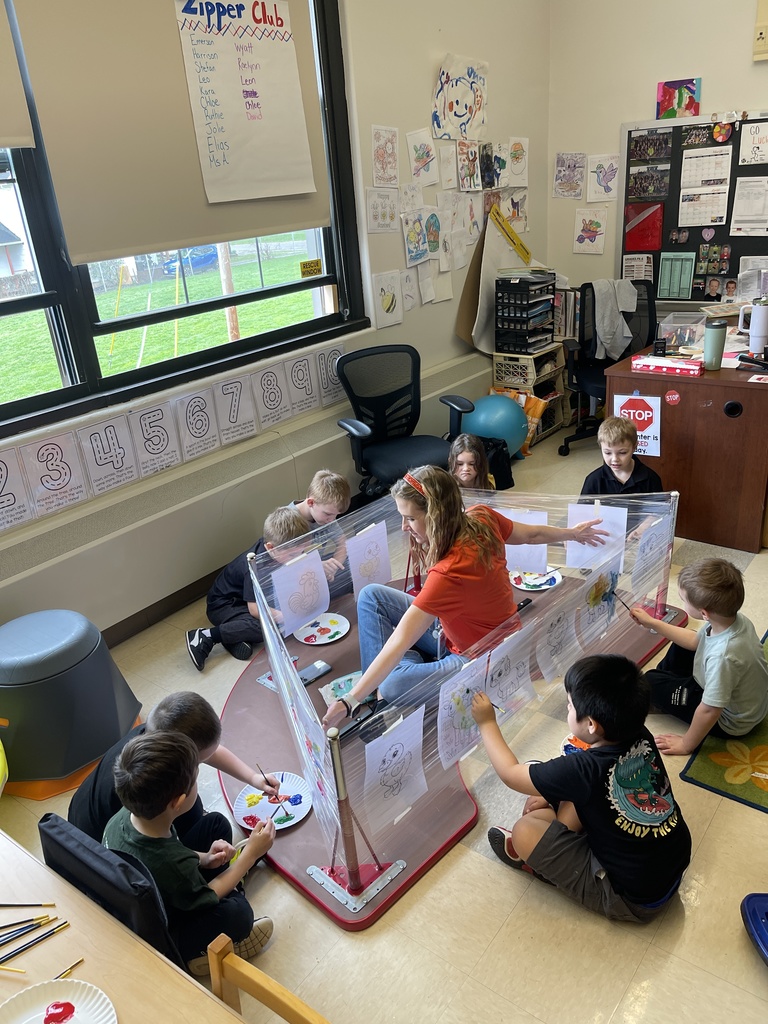students and teacher sitting on the floor with paint and worksheets
