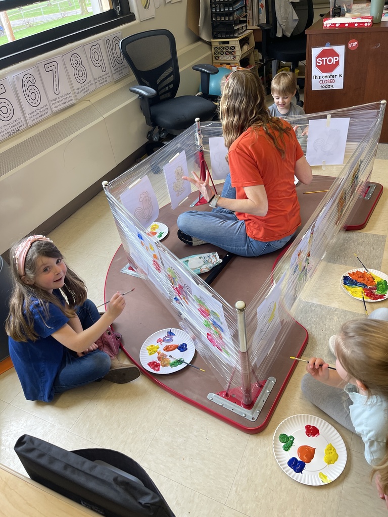teacher and students sitting on the floor with paint and worksheets