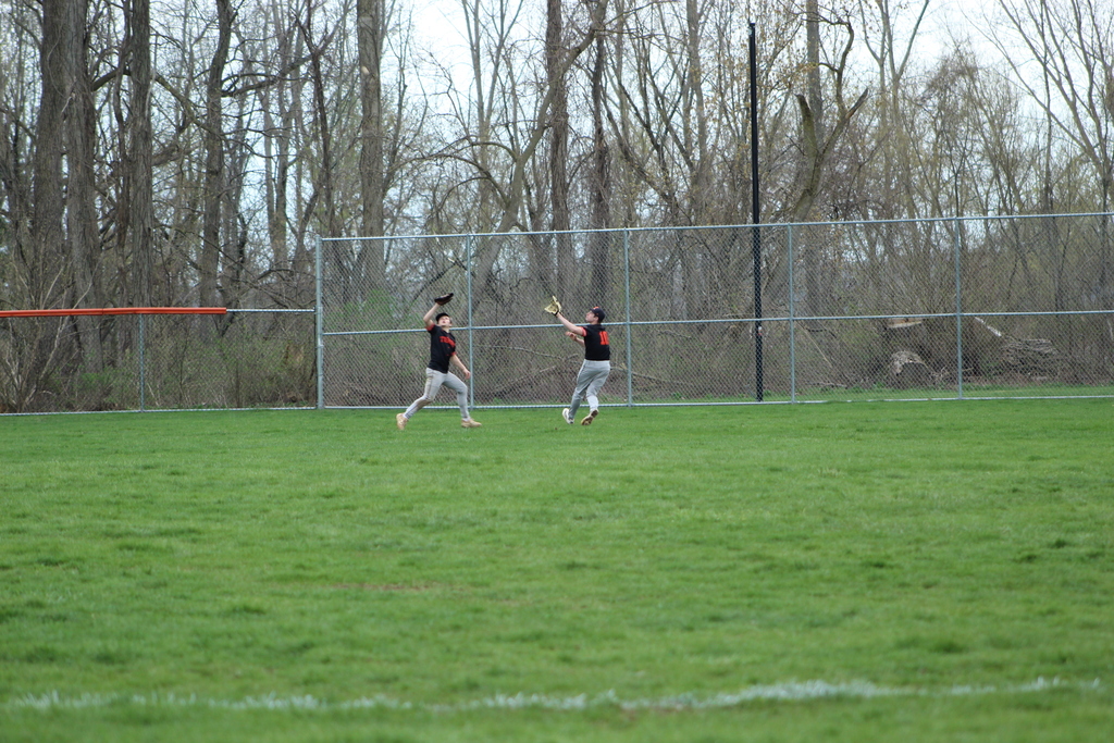 two boys trying to catch baseball in outfield