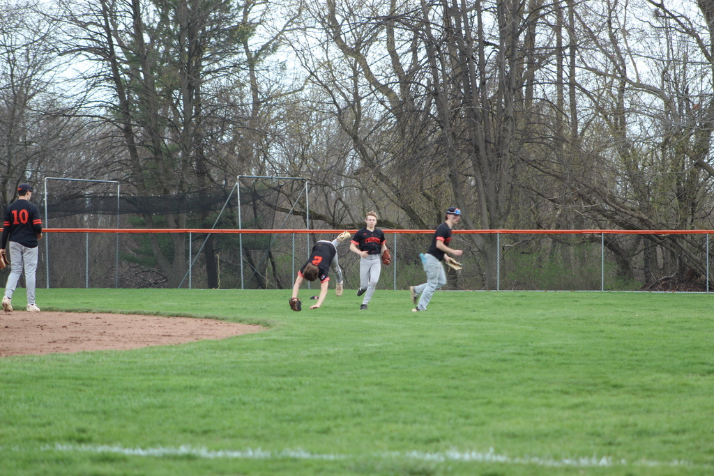 three boys trying to catch baseball in outfield