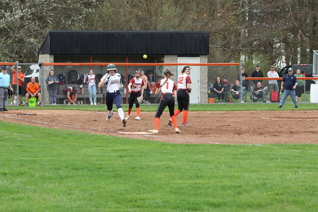 girl throwing softball to another girl guarding first base as runner approaches in softball game