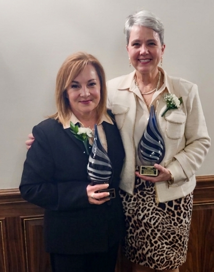 two ladies standing together holding awards