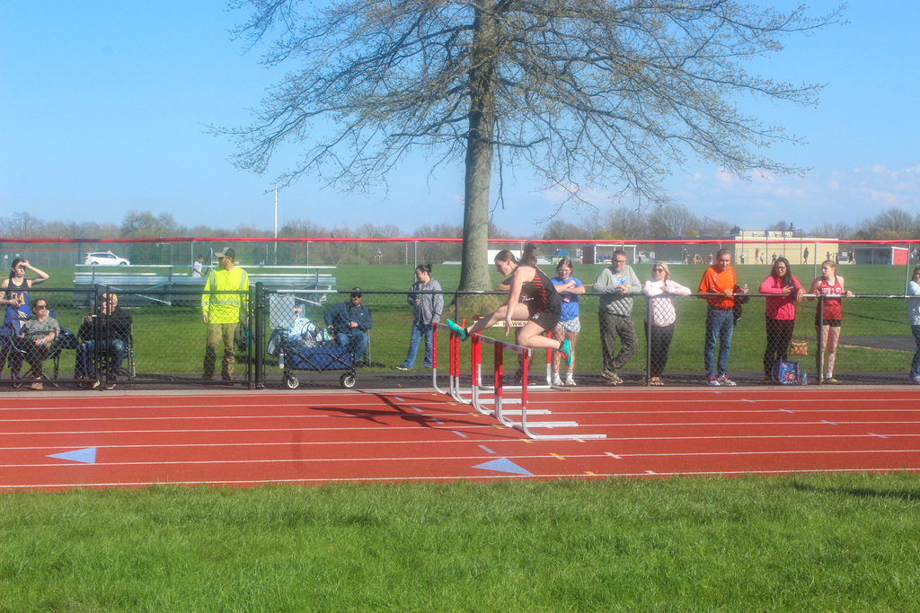 girl jumping over hurdle on track