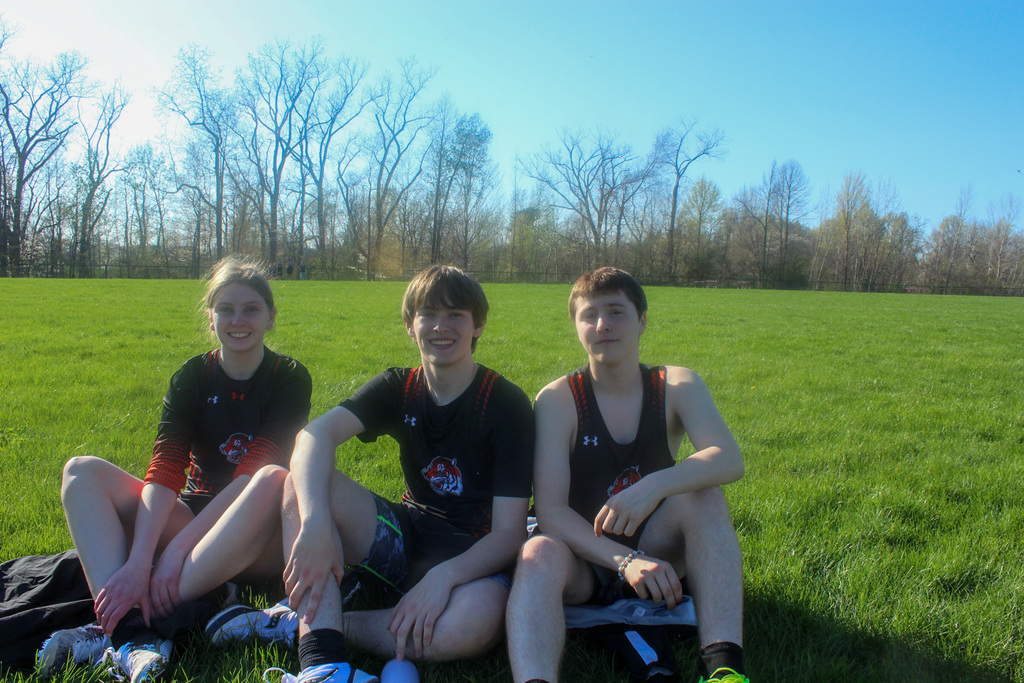 three students in track uniforms sitting together on grass